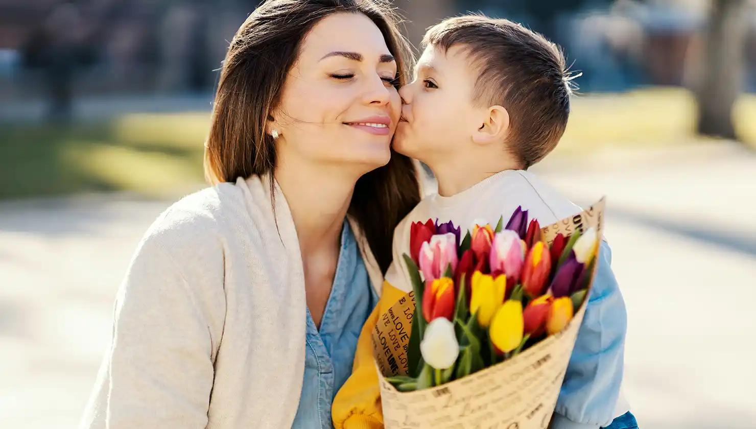 Mom being kissed by toddler son and holding tulips