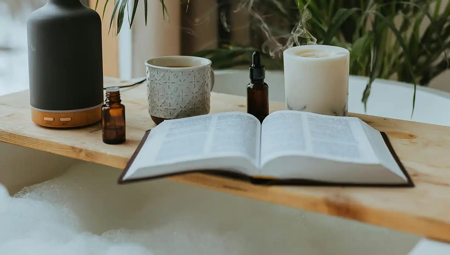 A calm, relaxed setting in a bubble bath with a book, candles, and aromatherapy