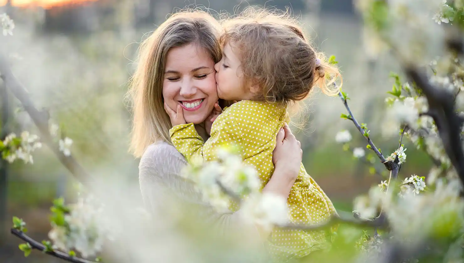 Potential mommy makeover patient receiving a kiss from her young daughter in nature