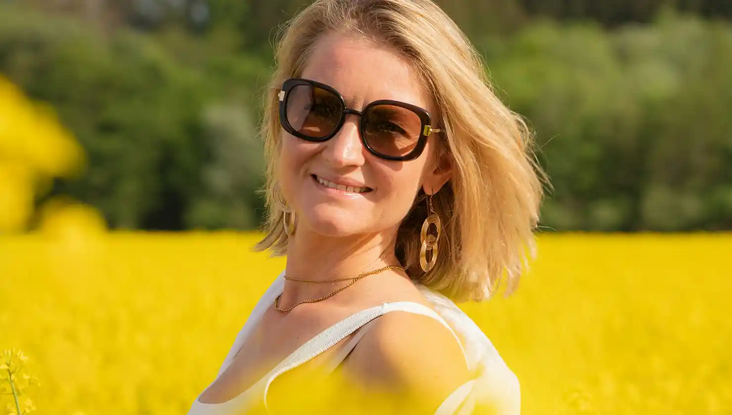 woman with large earrings in a field of flowers outside smiling - potential patient for earlobe repair